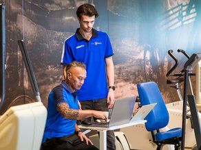 Twee medewerkers van MTC Zoetermeer achter een computer in de sportzaal.