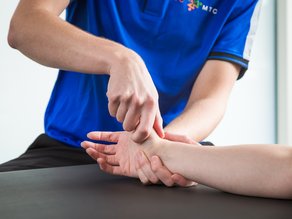 Fysiotherapeut van MTC Zoetermeer die de hand van een patiënt behandelt tijdens handfysiotherapie.