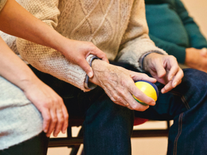 Geriatrie fysiotherapeut begeleidt oudere met bal tijdens oefening