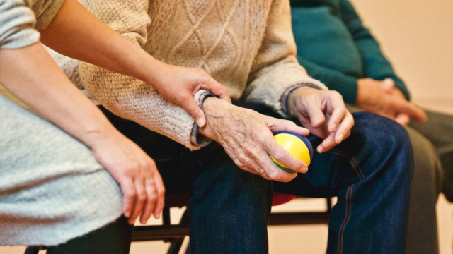 Geriatrie fysiotherapeut begeleidt oudere met bal tijdens oefening