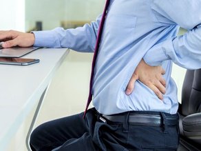 Man achter bureau met hand op rug, rugklachten bij bedrijfsfysiotherapie