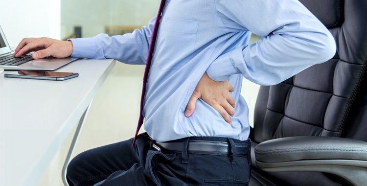 Man achter bureau met hand op rug, rugklachten bij bedrijfsfysiotherapie